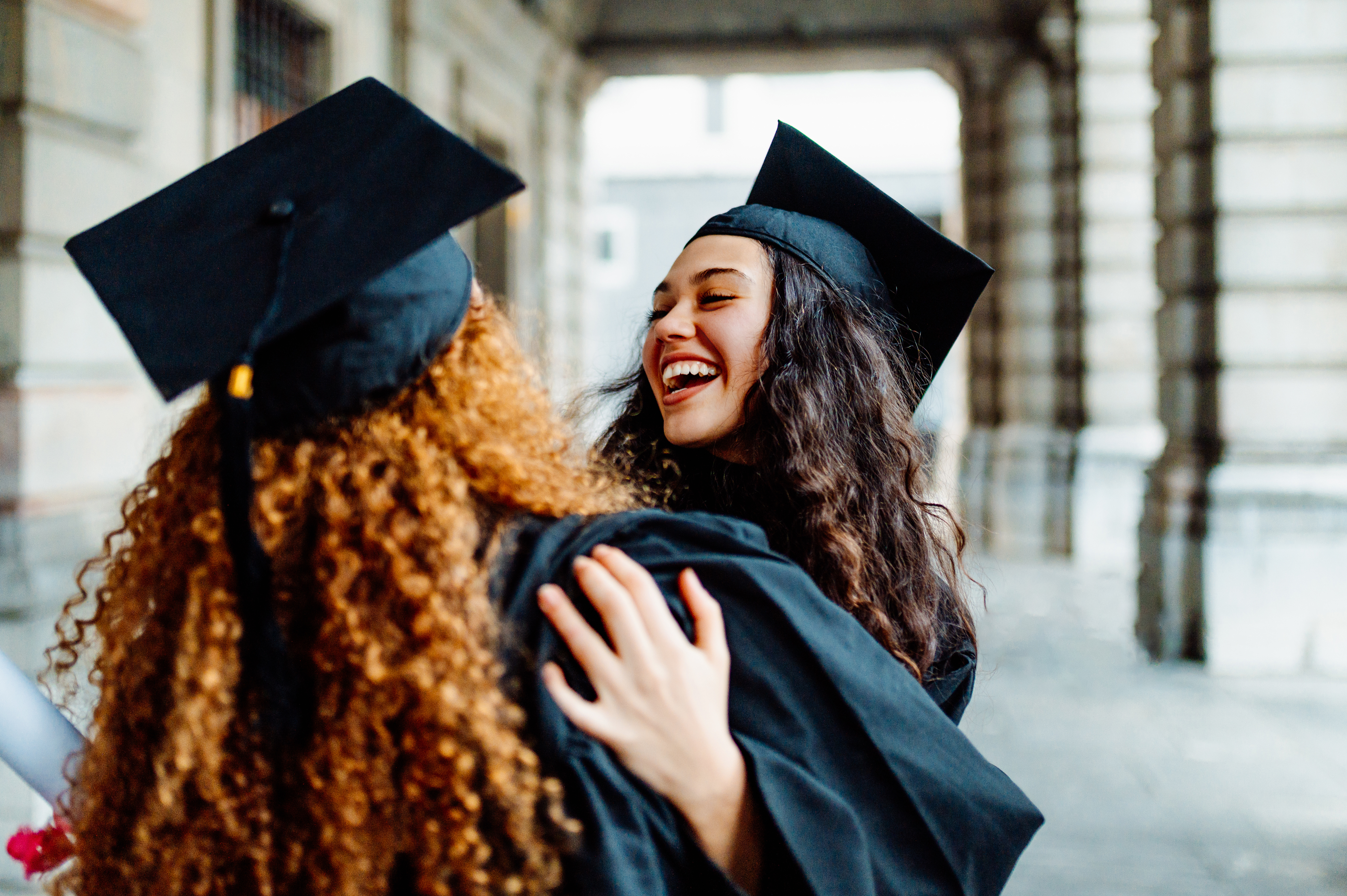 Two women in graduation caps embracing, celebrating educational achievement and future financial empowerment