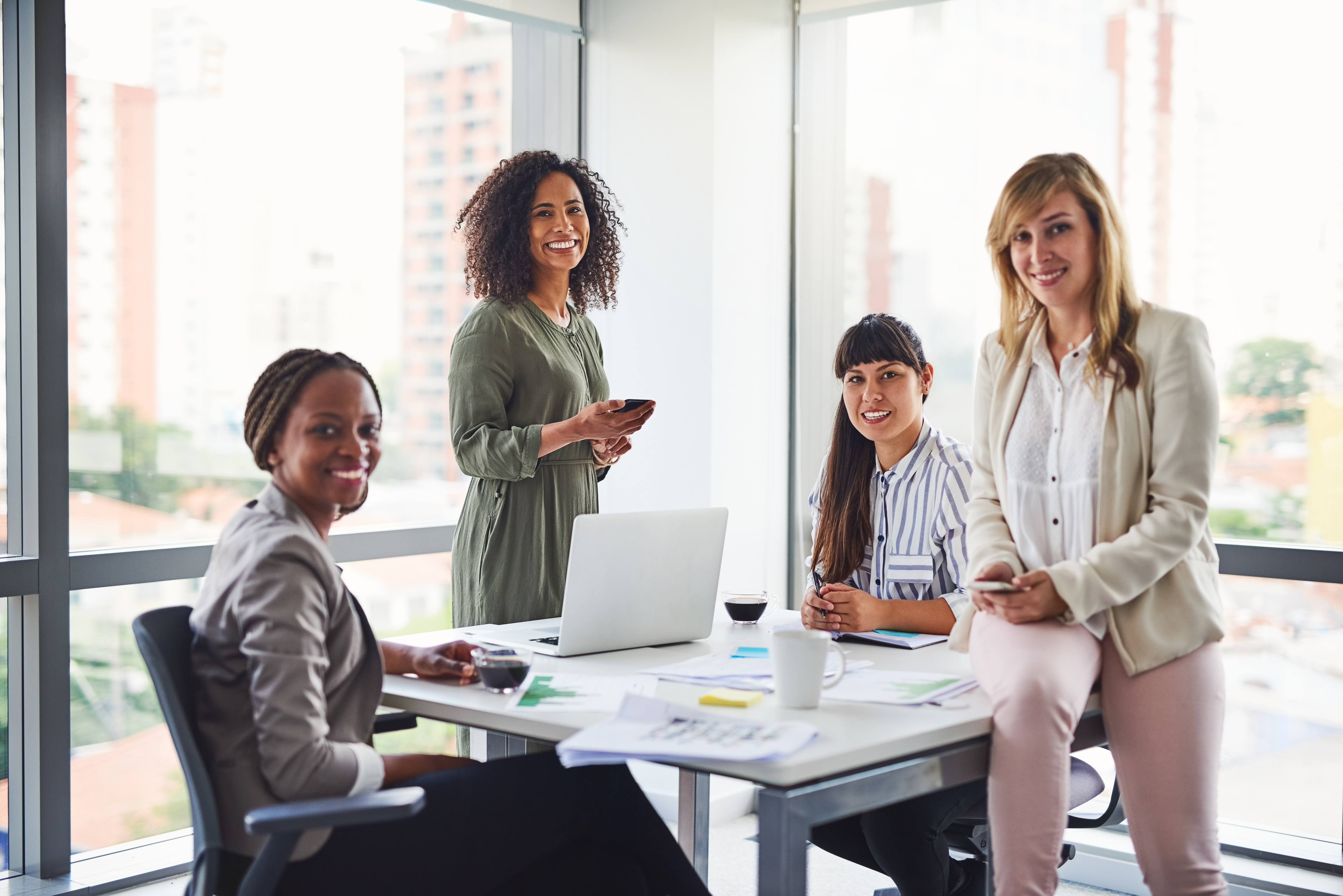 A diverse group of businesswomen around a table in a bright office, highlighting teamwork and financial collaboration.