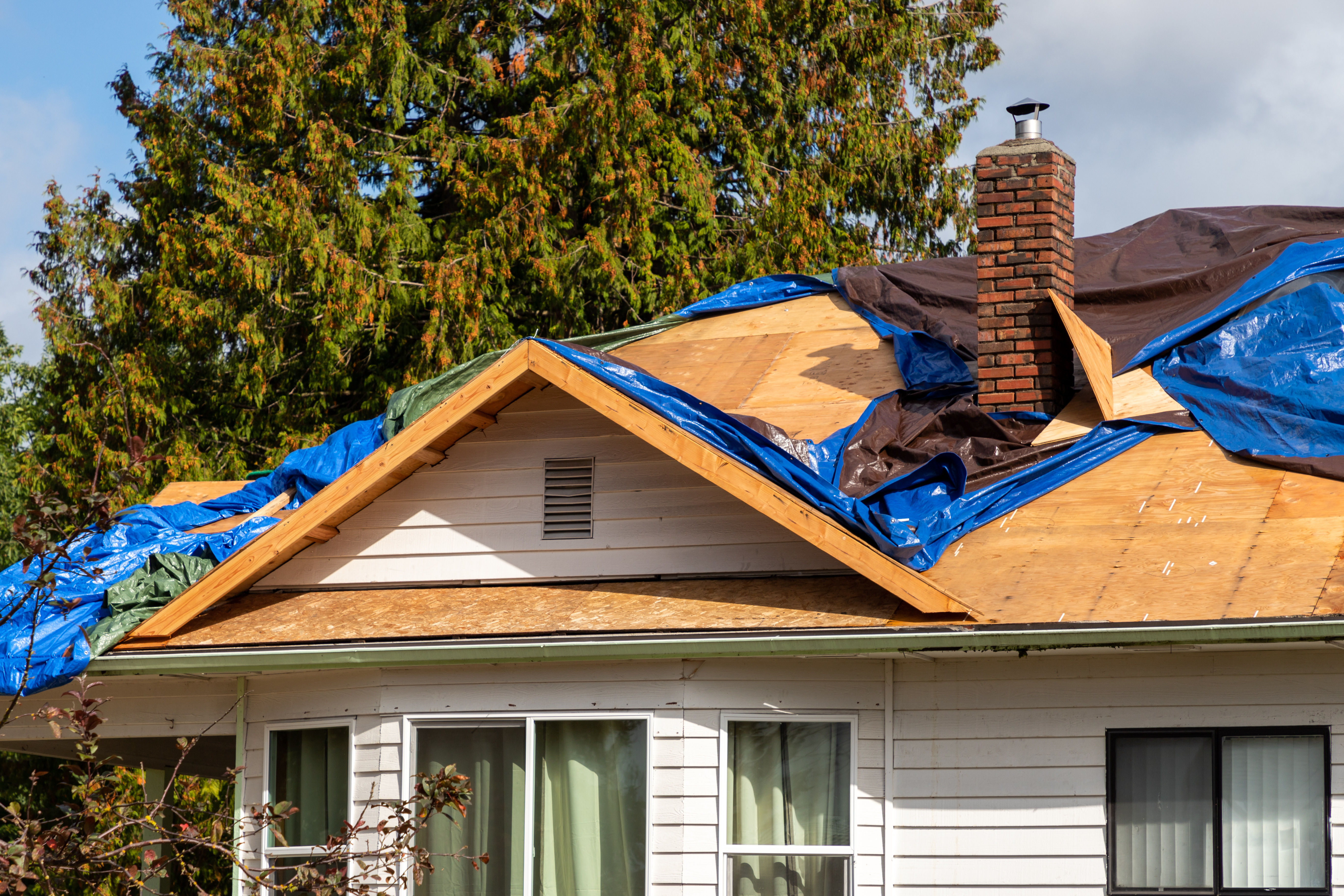 House with roof damage covered by tarps, illustrating sudden home repair emergencies