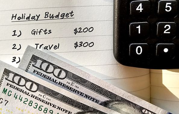 Notebook labeled Holiday Budget with calculator and cash illustrating organized holiday spending plan