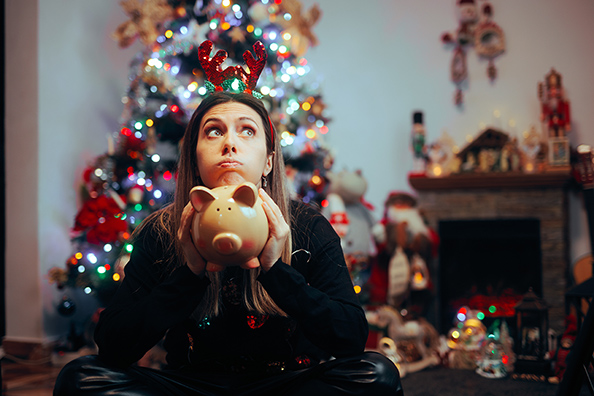 Woman holding piggy bank in front of Christmas tree representing holiday savings and financial mindfulness