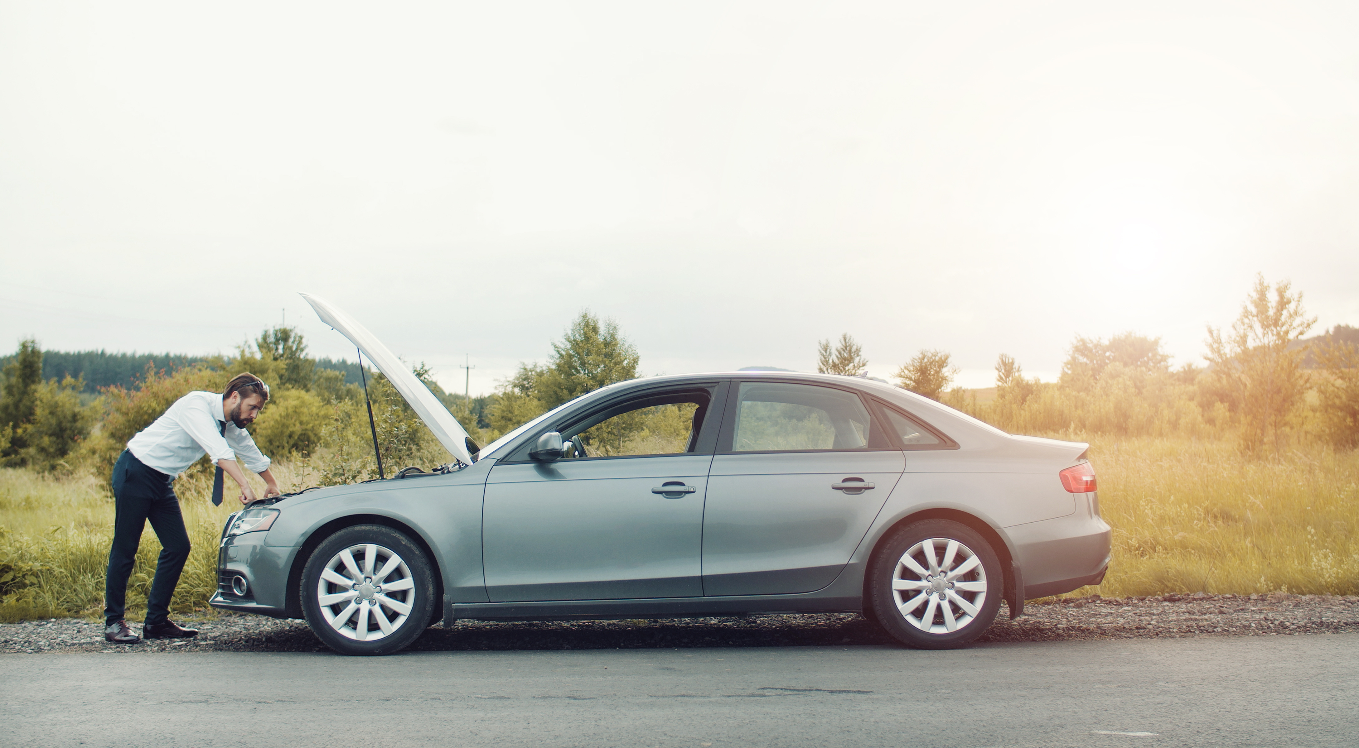 Man standing beside a broken-down car with the hood open, representing unexpected emergency expenses.