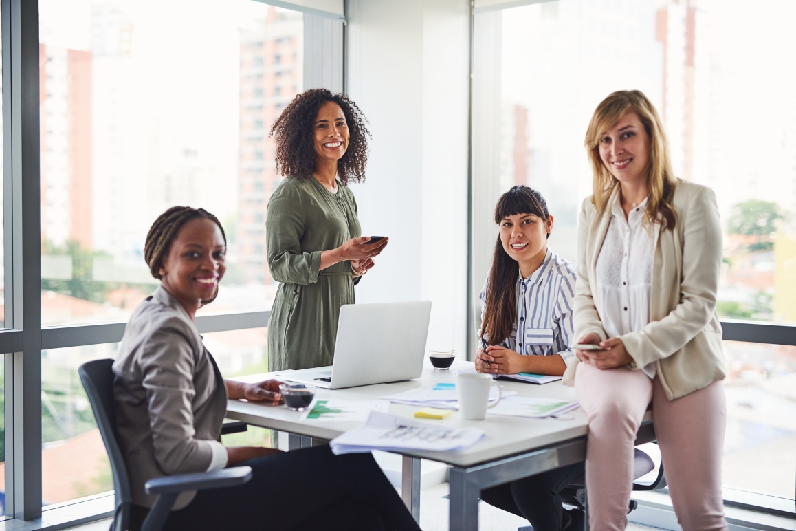 A diverse group of businesswomen around a table in a bright office, highlighting teamwork and financial collaboration.