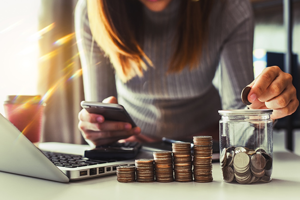 Woman stacking coins beside laptop and phone representing year-end financial planning and savings goals