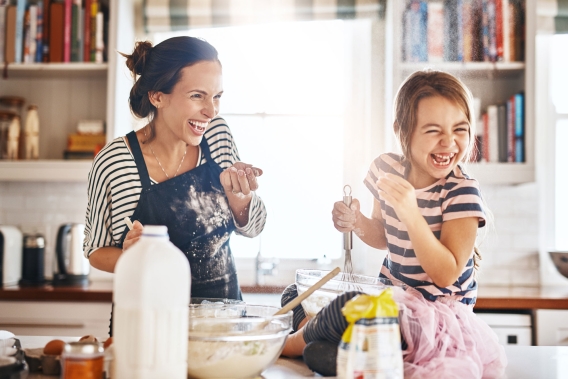 A mother and daughter smiling while baking in their home's kitchen. 